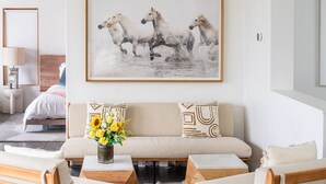 Een moderne woonkamer met een bank, twee fauteuils, een salontafel en een schilderij van paarden.