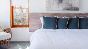 Een moderne slaapkamer met een groot bed, een houten hoofdbord en uitzicht door een raam.