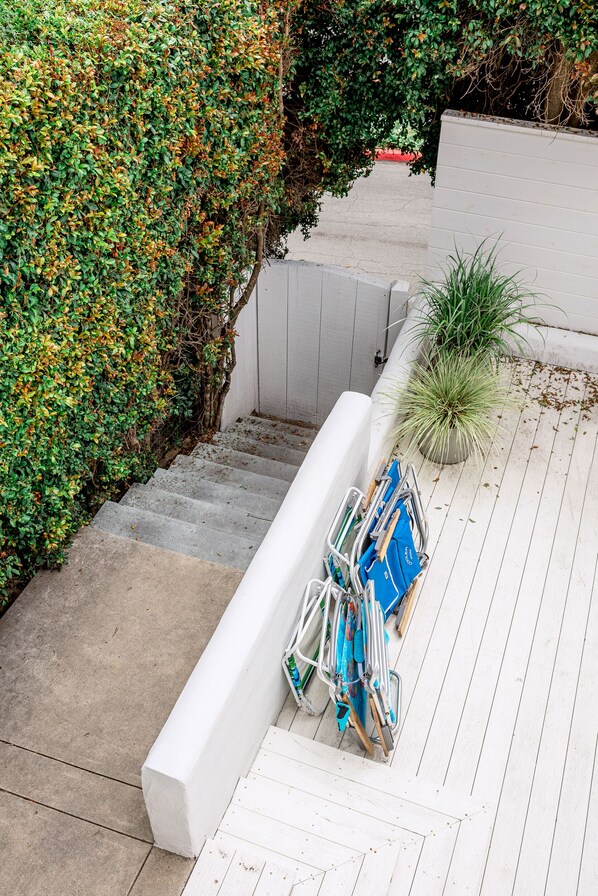 Un escalier menant à une terrasse dotée d’une rambarde blanche, d’un pot de fleurs et d’un support à vélos où sont entreposés des objets.