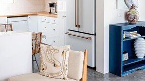 Een moderne keuken met witte kasten, een roestvrijstalen koelkast en een blauwe boekenkast.