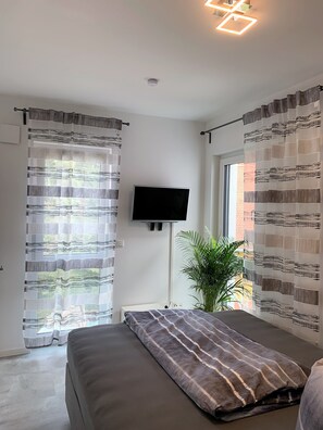 Relax in a serene space with a comfortable bed, flat-screen TV, and a view of lush greenery.
