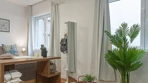 Een moderne woonkamer met een houten bureau, een staand spiegel, een potplant en uitzicht op de omgeving.