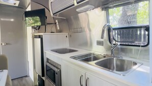 A compact kitchen with a sink, stove, and ventilation hood. - Airstream Escape + Pool + Fenced Yard (Austin)