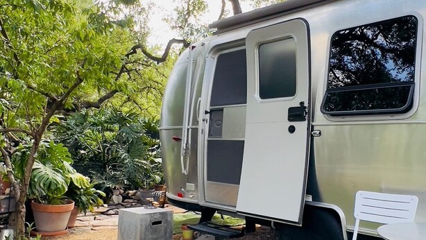 A silver recreational vehicle parked in a garden with a white chair and a concrete block. - Airstream Escape + Pool + Fenced Yard (Austin)