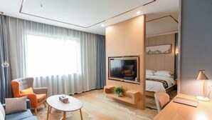 Una moderna camera d'albergo con divano, tavolino rotondo, televisore a parete, un letto e una scrivania con lampada.