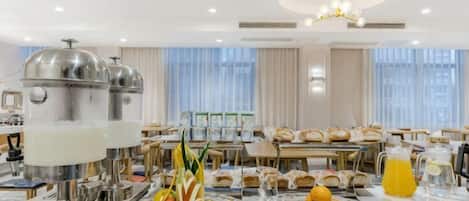 A hotel breakfast area with a buffet setup, including a variety of fruits and beverages.