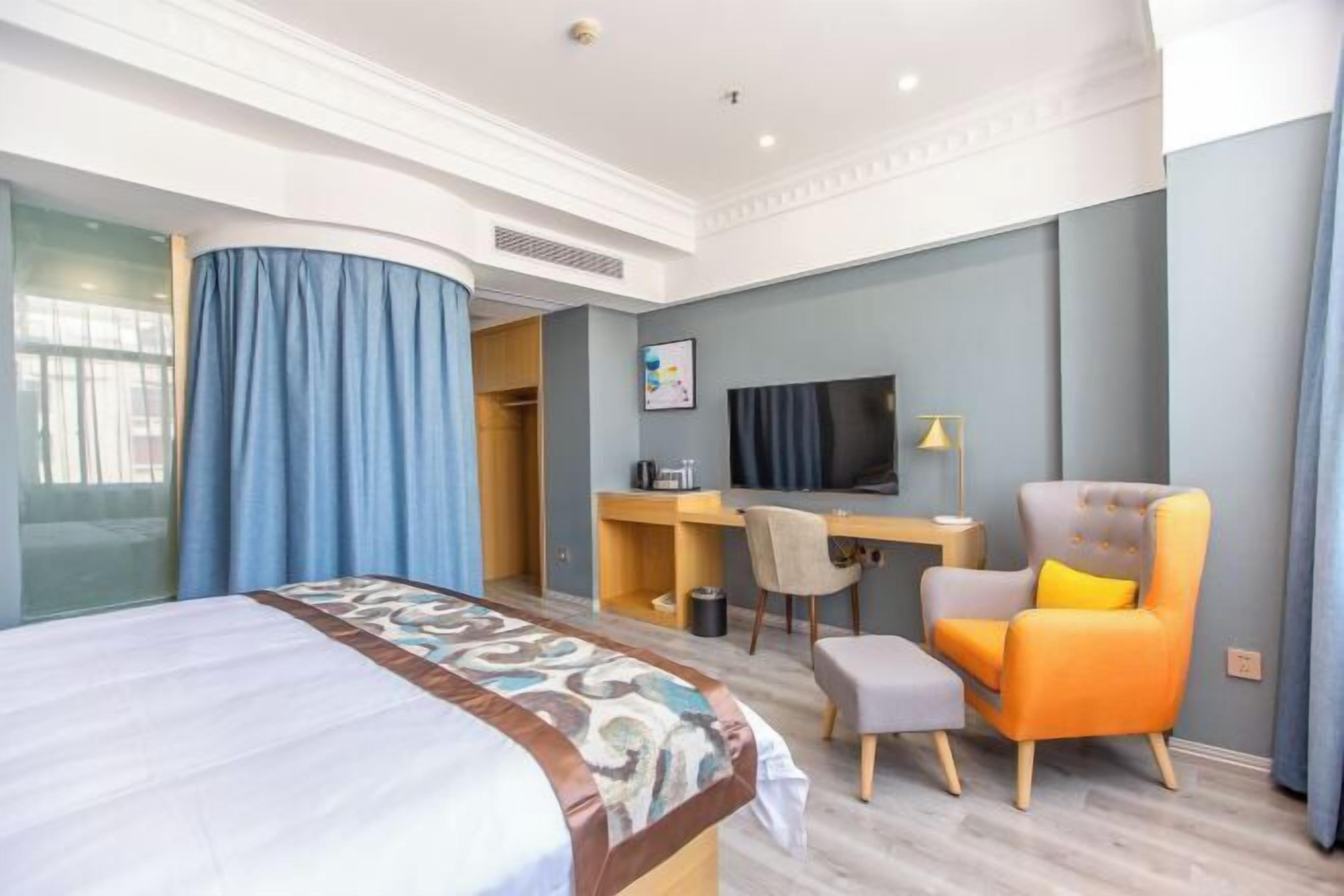Habitación de hotel con cama, escritorio, silla, televisor y una mesita.