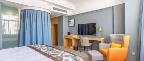 Habitación de hotel con cama, escritorio, silla, televisor y una mesita.