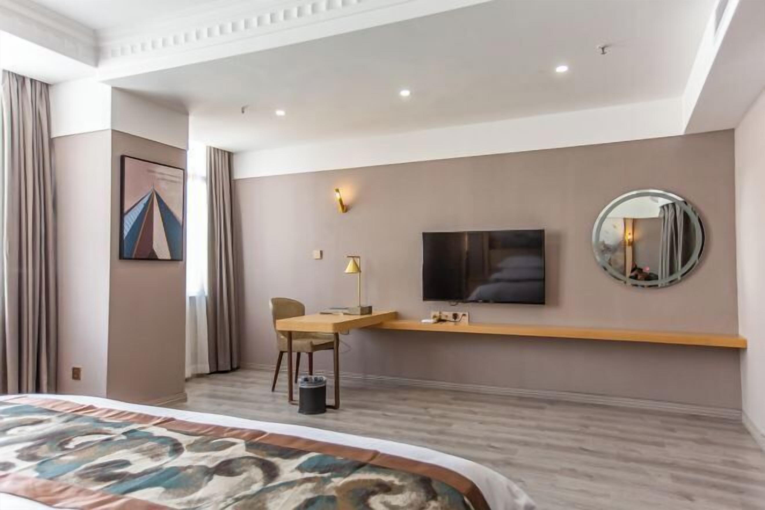 A hotel room with a bed, a desk, a chair, a TV, a mirror, and a painting on the wall.