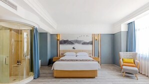 Una camera d'albergo con un letto grande, un box doccia in vetro, una poltrona e un quadro appeso al muro.