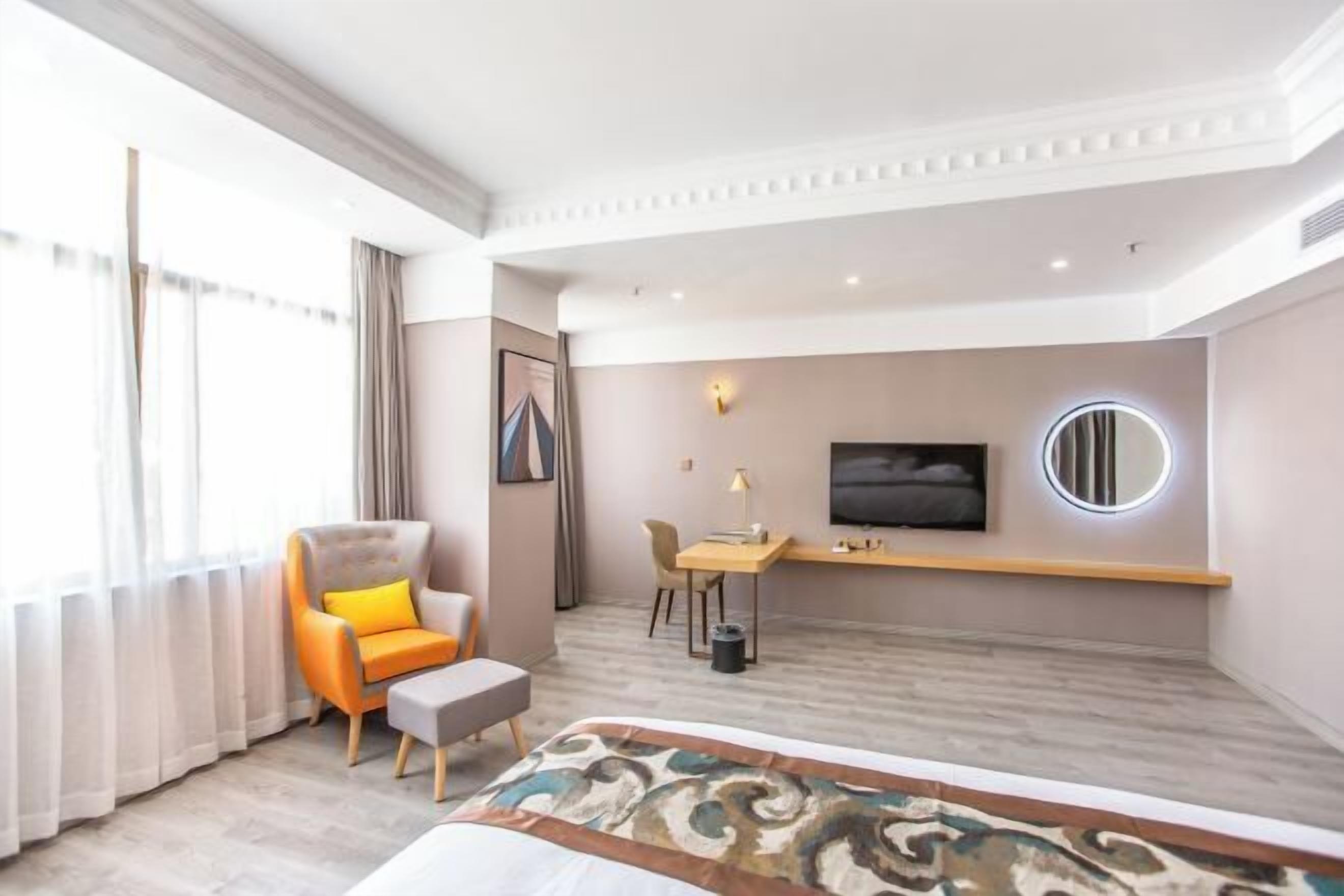 A hotel room with a bed, a desk, a chair, a television, and a window with curtains.
