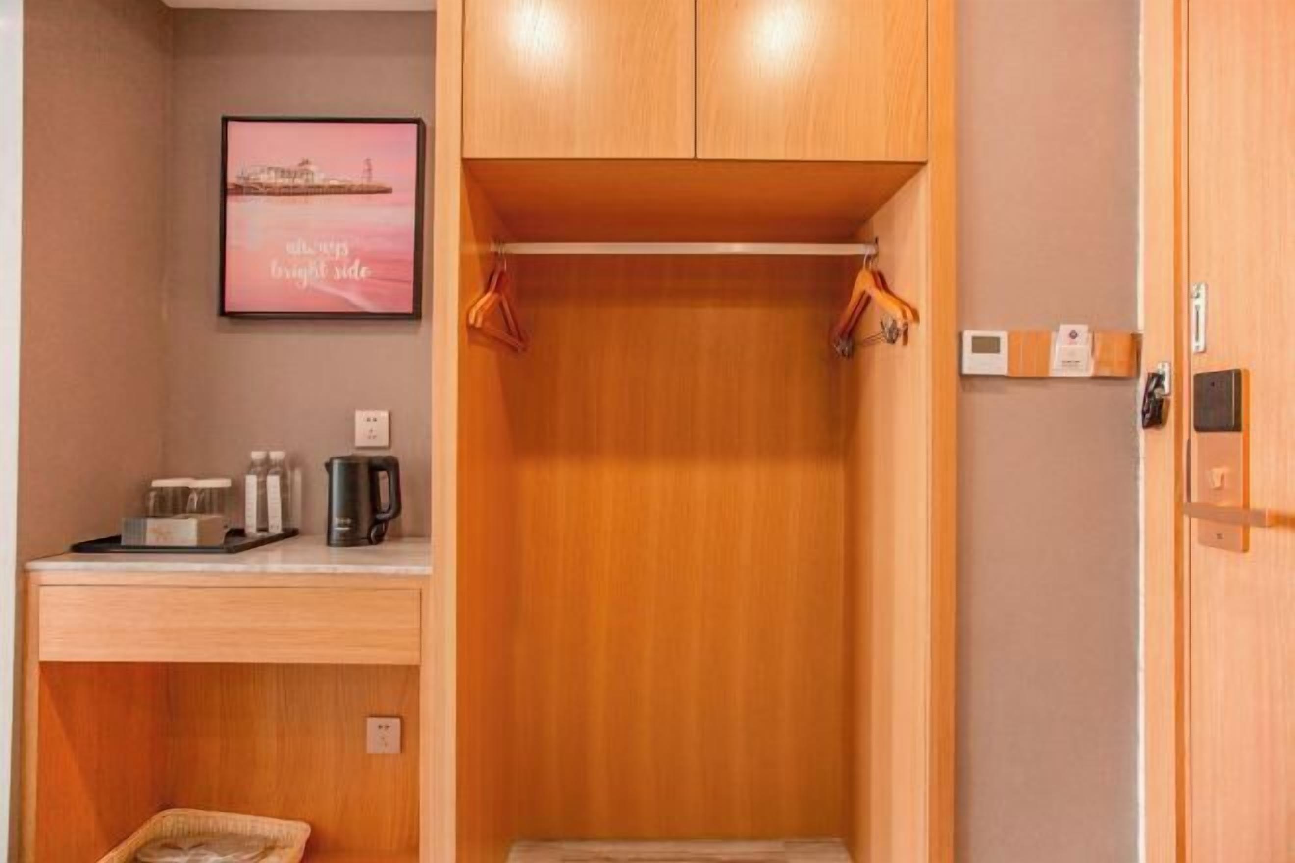 A hotel room with a wooden wardrobe, a small desk with a coffee maker, and a framed picture on the wall.