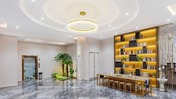 Una hall moderna con pavimento in marmo, un lampadario al centro, un’area salotto con un tavolo e una grande libreria.