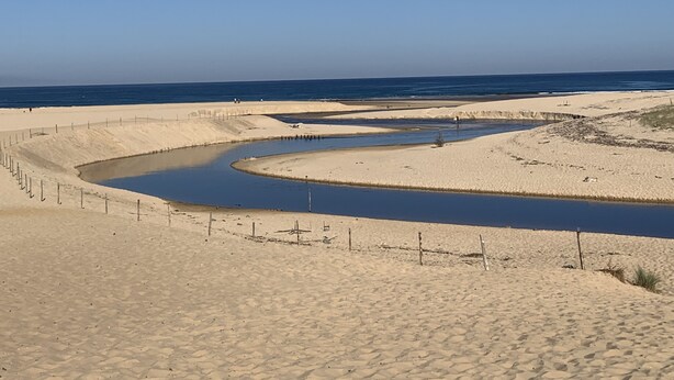 Paisaje desértico con un canal serpenteante, dunas arenosas y un cielo azul despejado.
