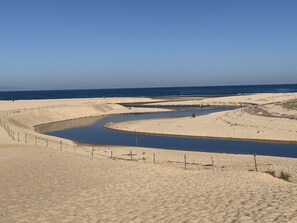 Wüstenlandschaft mit einem gewundenen Wasserkanal, Sanddünen und blauem Himmel.