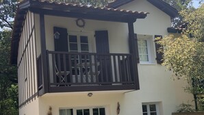 Una casa de dos pisos con un balcón, un patio con mesa y sillas, y un pequeño jardín.