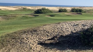 Un campo de golf con búnkeres de arena, calles verdes y una vista despejada del océano.