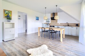 A modern kitchen with a wooden dining table and chairs, a white cabinet, and a hanging light fixture. - Beautiful vacation apartment. Top floor near the beach & quiet location to relax (Gaski)