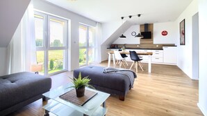 A modern living room with a sofa, a glass coffee table with a plant, and a dining area with a table and chairs. - Beautiful vacation apartment. Top floor near the beach & quiet location to relax (Gaski)