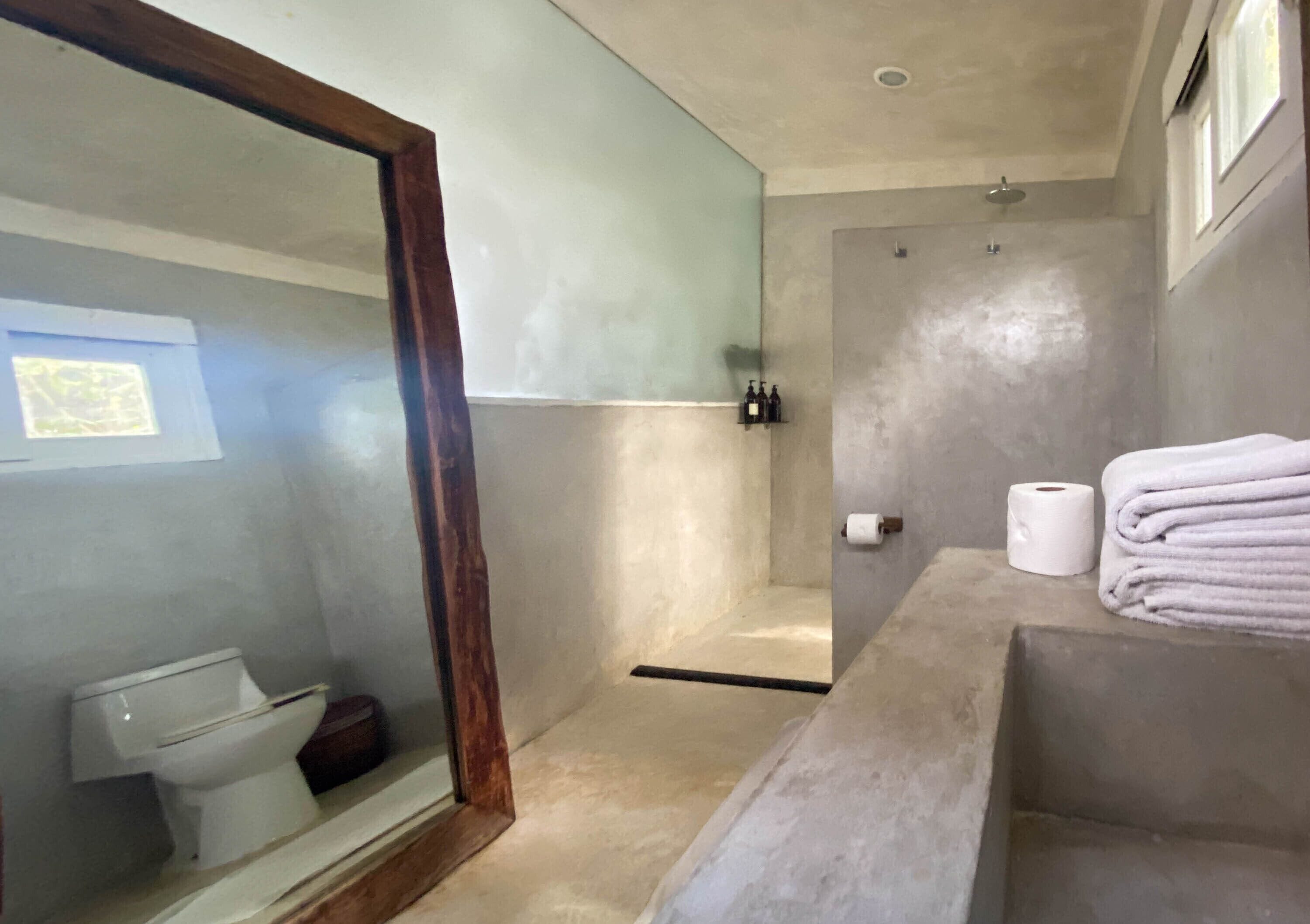 A bathroom with a glass shower enclosure, a toilet, a sink with a towel stack, and a visible window.