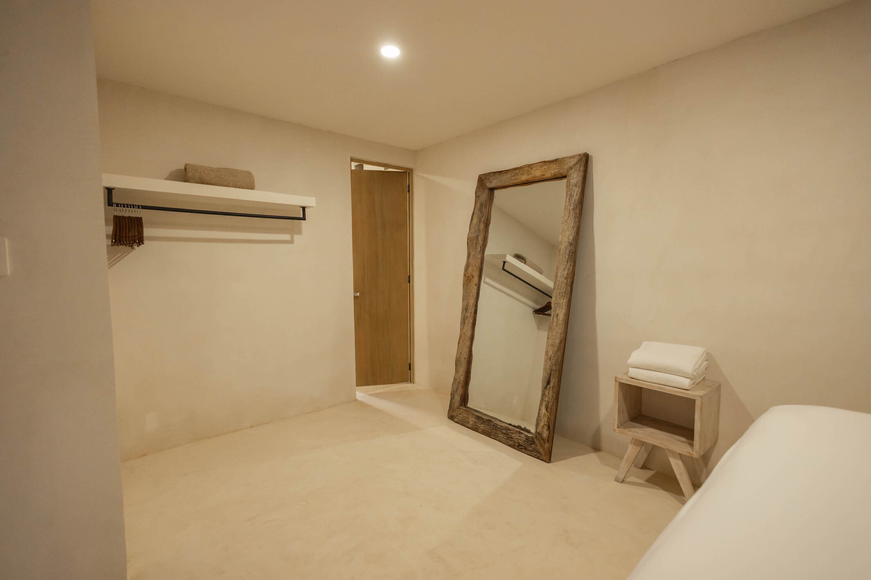 A bedroom with a large mirror, a bedside table, a shelf with a towel, and a door leading to another room.