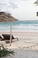 A beach with a thatched-roof structure and lounge chairs.