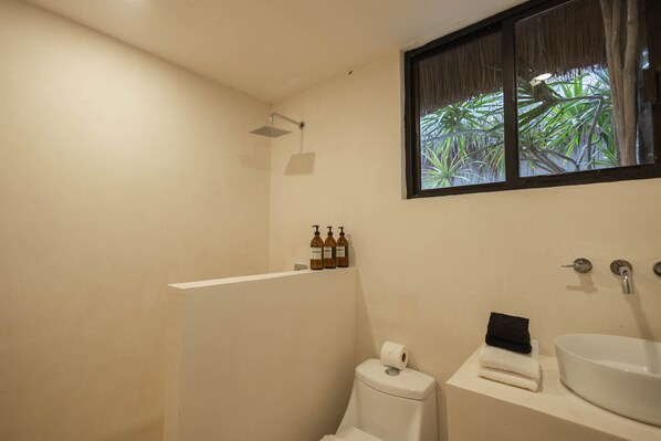 Un baño con ducha, inodoro, lavamanos y ventana con vistas a la vegetación.
