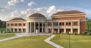 A large, modern building with a central rotunda, multiple wings, and a well-maintained lawn.