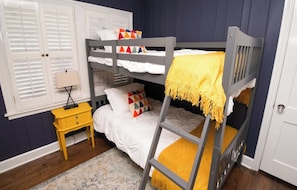 A bunk bed room with a ladder, a bedside table, and a window with shutters.