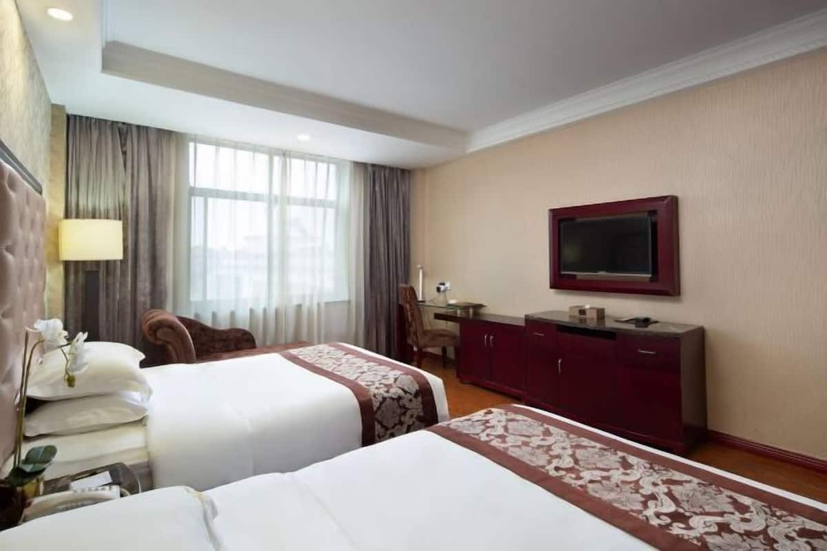 Ein Hotelzimmer mit zwei Betten, einem Schreibtisch, einem Fernseher und einem großen Fenster mit Vorhängen.