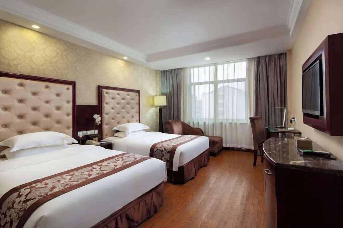 Ein Hotelzimmer mit zwei Betten, einem Schreibtisch, einem Sessel und einem Fernseher.
