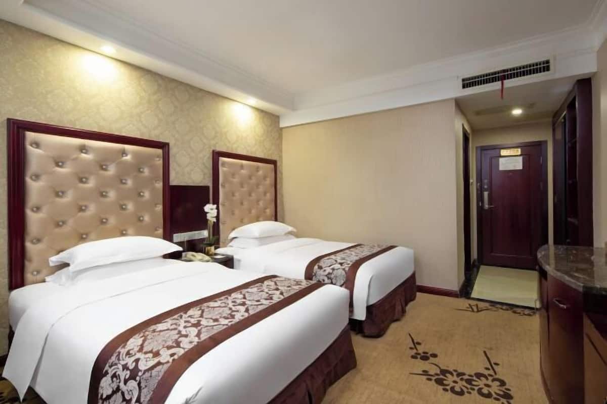 Ein Hotelzimmer mit zwei Betten, einem Holzkopfende, einem Nachttisch und Teppichboden.