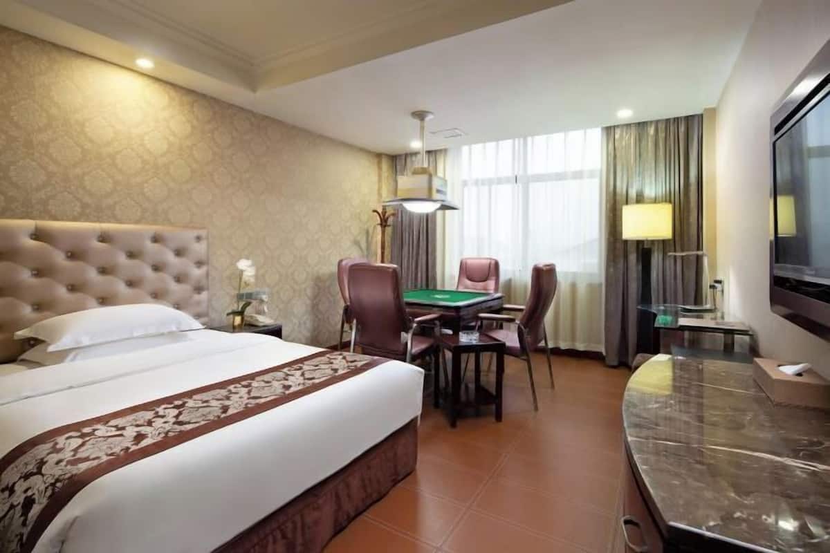 Ein Hotelzimmer mit einem großen Bett, einem Schreibtisch mit Stuhl, einem Fernseher und einem Fenster mit Vorhängen.