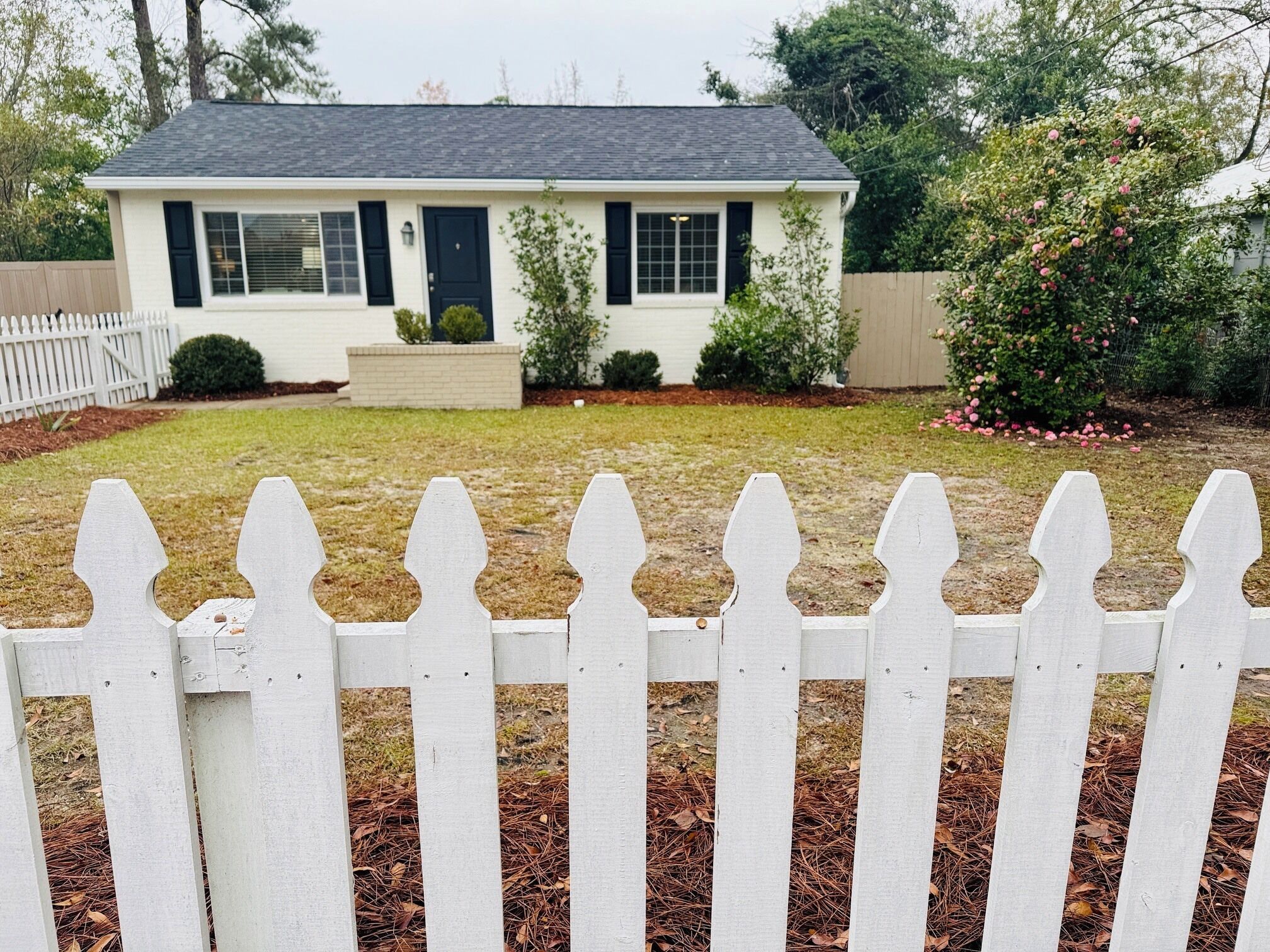 A single-story house with a white picket fence in the foreground.