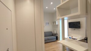 A modern living room with a grey sofa, a flat-screen TV mounted on the wall, and a white coffee table. - Small and cozy studio apartment in the center of Florence (FIRENZE)