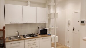 A small kitchen with white cabinets, a gas stove, a microwave, and a sink. - Small and cozy studio apartment in the center of Florence (FIRENZE)