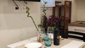 A dining area with a white table, chairs, a TV mounted on the wall, and a window with sheer curtains. - Small and cozy studio apartment in the center of Florence (FIRENZE)