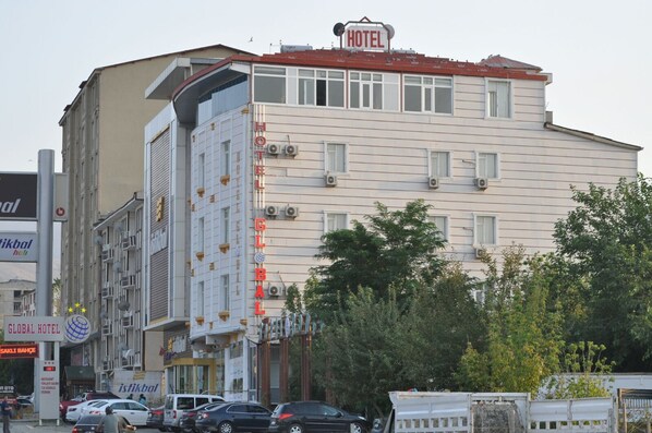 Ett hotell med ett rött tak och flera våningar. Flera bilar är parkerade framför, och en skylt med texten ”Global Hotel” syns.
