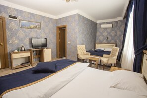 Ett hotellrum med en stor säng, två fåtöljer, ett litet skrivbord med en tv och en minibar.