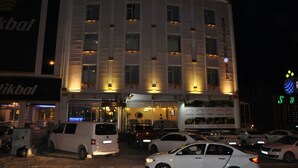 A multi-story hotel with a curved facade, multiple windows, and a parking lot with several cars. - GLOBAL OTEL (Mus)