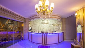 A reception area with a chandelier, a reception desk labeled "GLOBAL," and a mirror on the right. - GLOBAL OTEL (Mus)