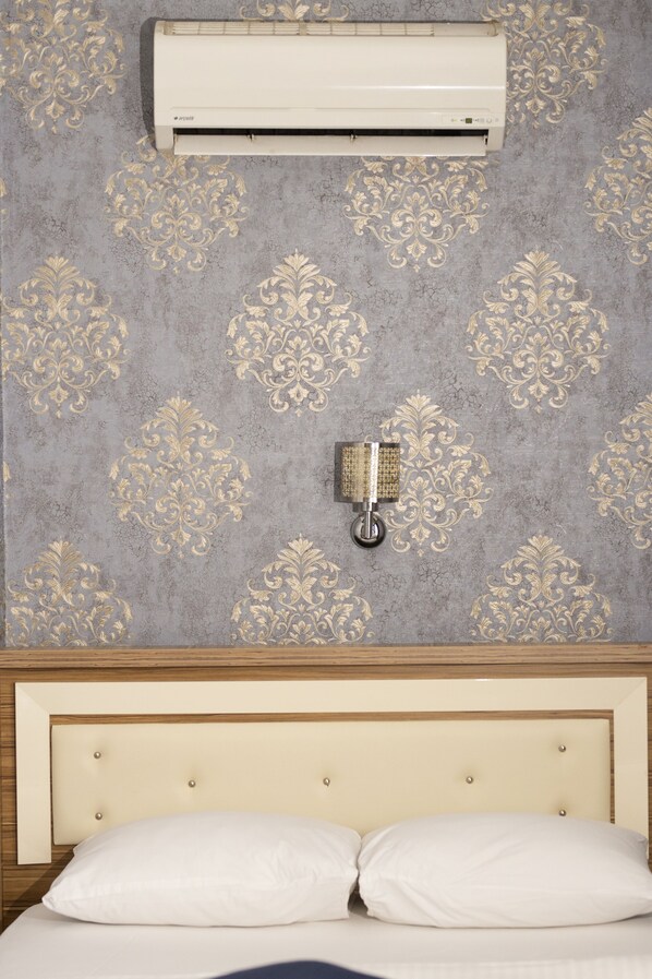 A bedroom with a bed, a wall-mounted air conditioner, and a wall-mounted light fixture.