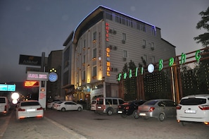 A hotel with a sign reading "HOTEL GLOBAL" and "SAKII" in neon lights. There are multiple cars parked in front, and the building has a modern design with large windows.