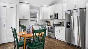 Una cocina moderna con armarios blancos, electrodomésticos de acero inoxidable y un comedor con sillas verdes y una mesa de madera.