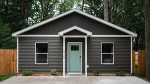 Una casa de dos pisos con fachada gris, puerta verde y pequeño jardín delantero.