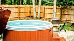 Un jacuzzi con revestimiento de madera, rodeado por una valla de madera, mobiliario exterior y árboles.