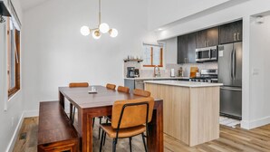 Uma cozinha moderna com uma ilha central, eletrodomésticos embutidos e uma área de jantar com mesa e cadeiras de madeira.