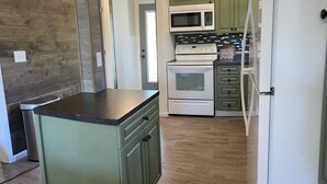 A kitchen with a central island, a microwave, an oven, and green cabinets. - The Capitol House-East Village/Downtown, King Bed (Des Moines)