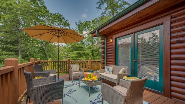 A wooden deck with wicker furniture, a table, and an umbrella. - Spacious Log Cabin in community with Lake and River Access. (Lake Lure)