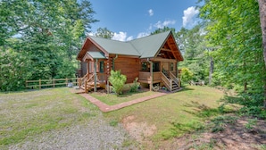 A wooden cabin with a porch, surrounded by trees and a gravel driveway. - Spacious Log Cabin in community with Lake and River Access. (Lake Lure)